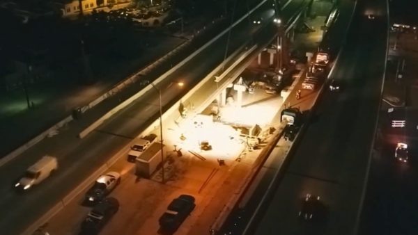 Crews shifted 10 bridge beams by truck onto the wide shoulder of the US 290 mainlanes, then crane operators lifted and set the beams on bearing pads (Still from a Balfour Beatty video)