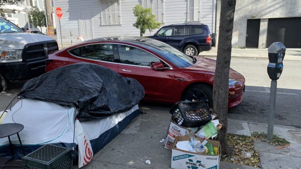 A homeless person’s encampment photographed last year in front of a parked Tesla in San Francisco’s Mission District (Carmen Esparza Amoux/CC BY-SA 4.0)